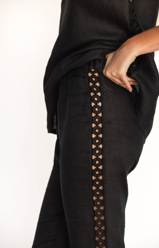 Close-up of Black linen trousers with sangallo embroidery along the sides, showing elasticated waistband and back zipper.