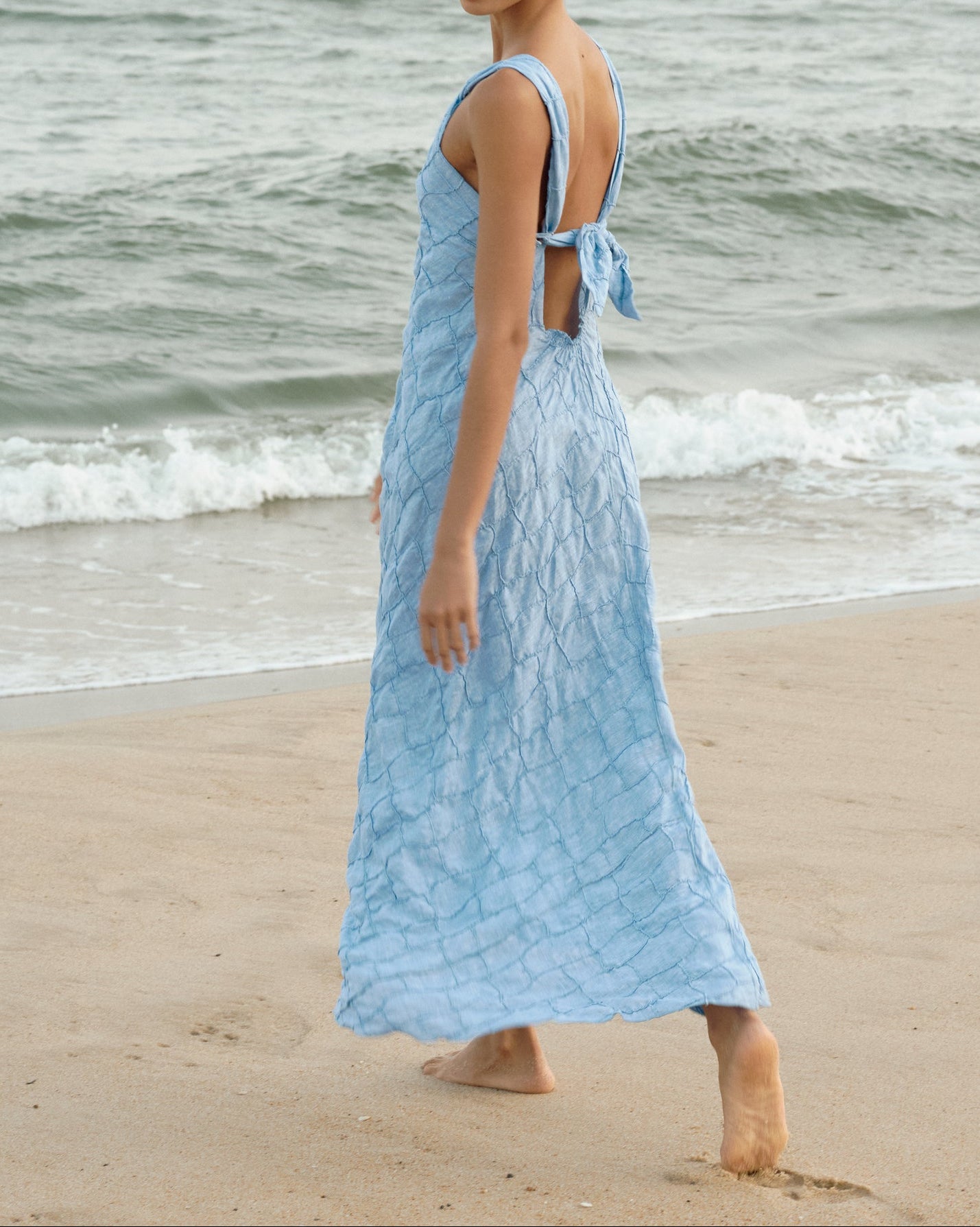 Woman in a Blue Jeans dress standing on a beach with ocean waves in the background