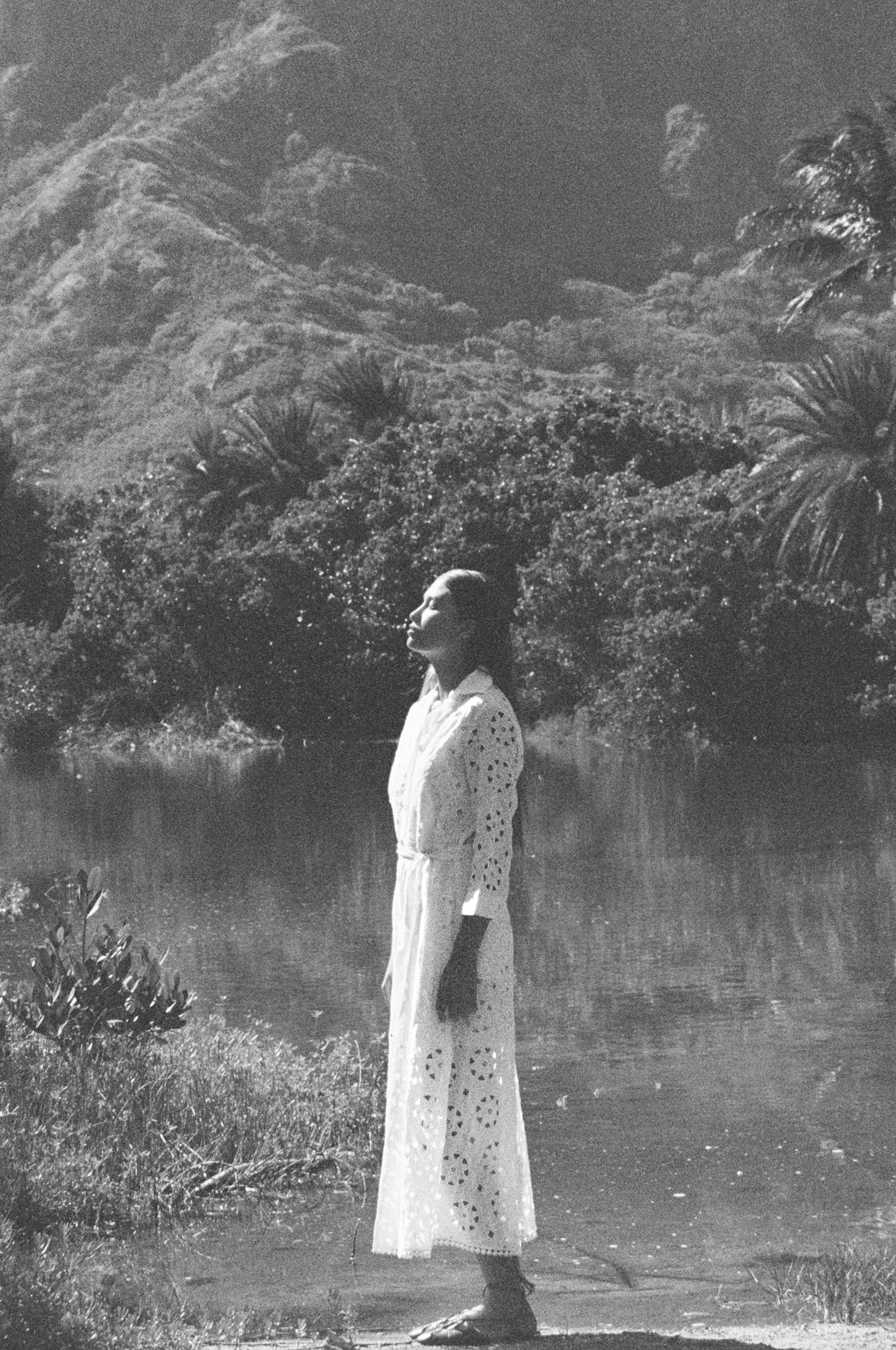 Person standing in a scenic location with mountains and palm trees in the background White