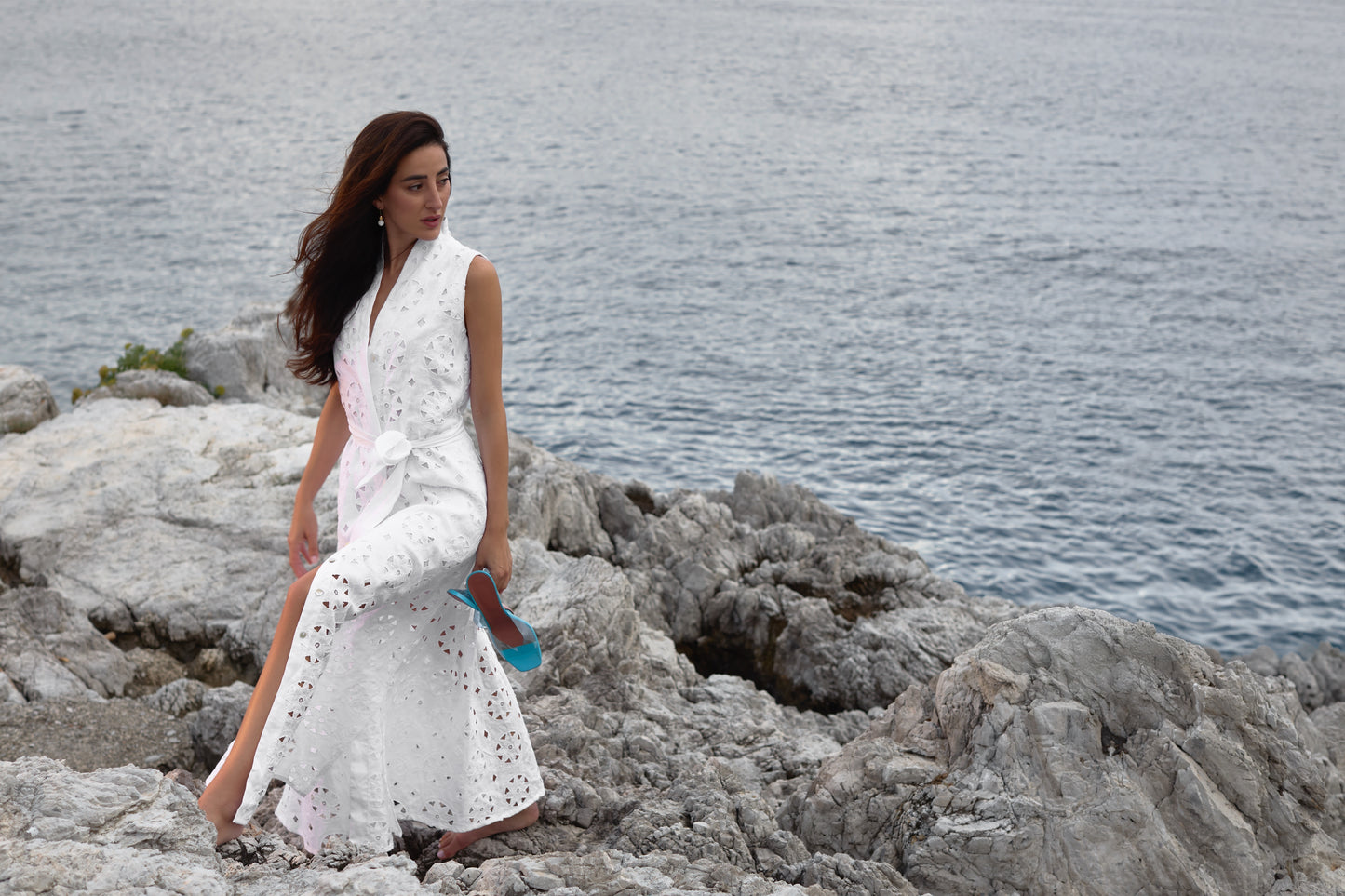 Woman in a White dress standing on rocky terrain by a body of water