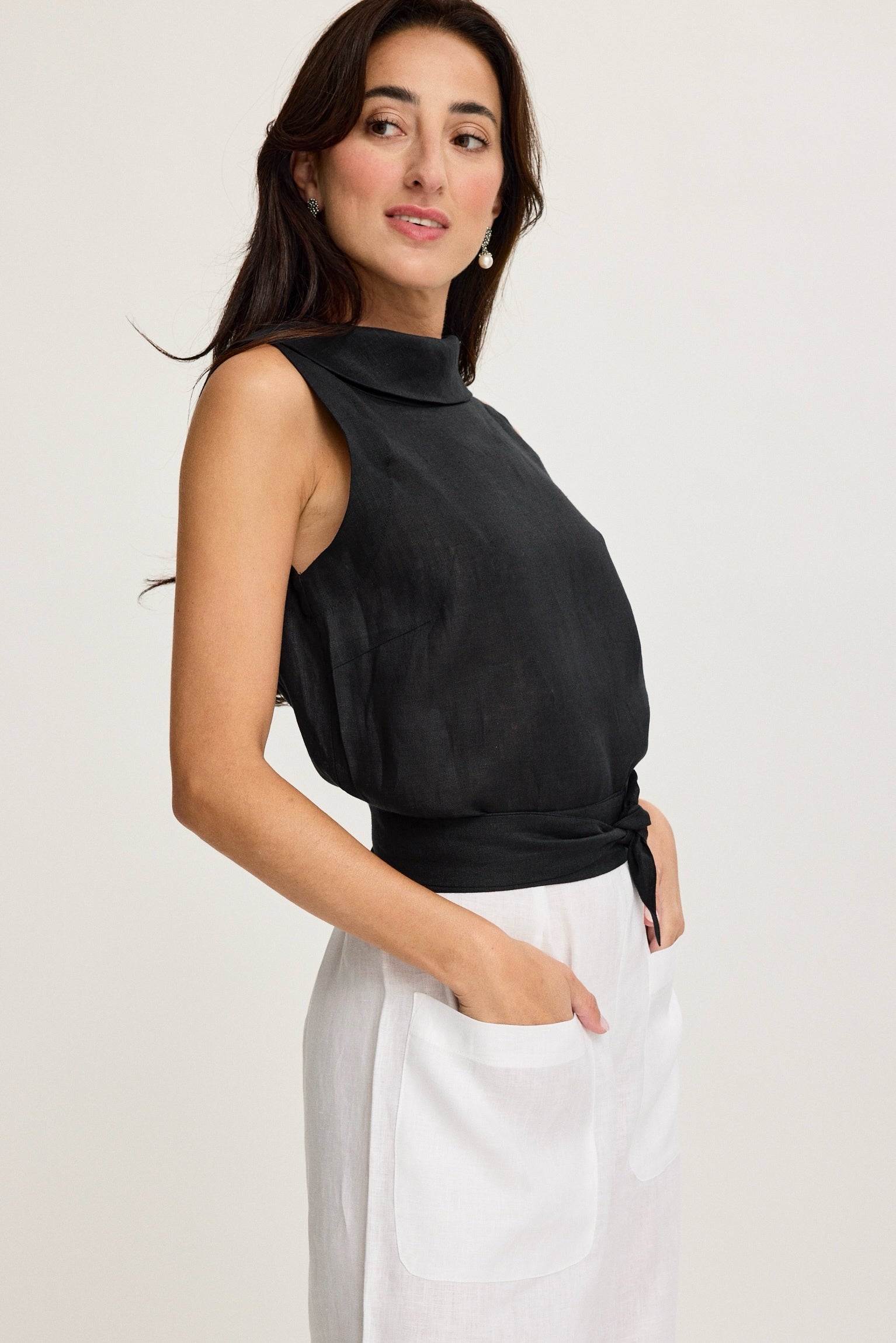 Woman wearing a black sleeveless top and white pants on a plain background Black & White