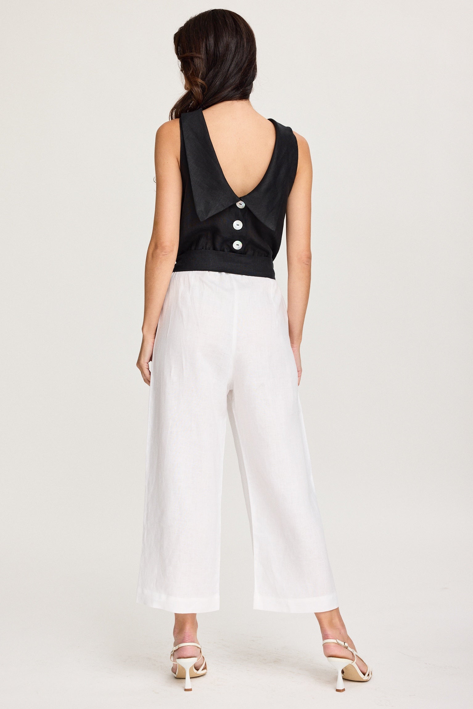 Woman wearing a black sleeveless top with buttons and white pants on a white background Black & White