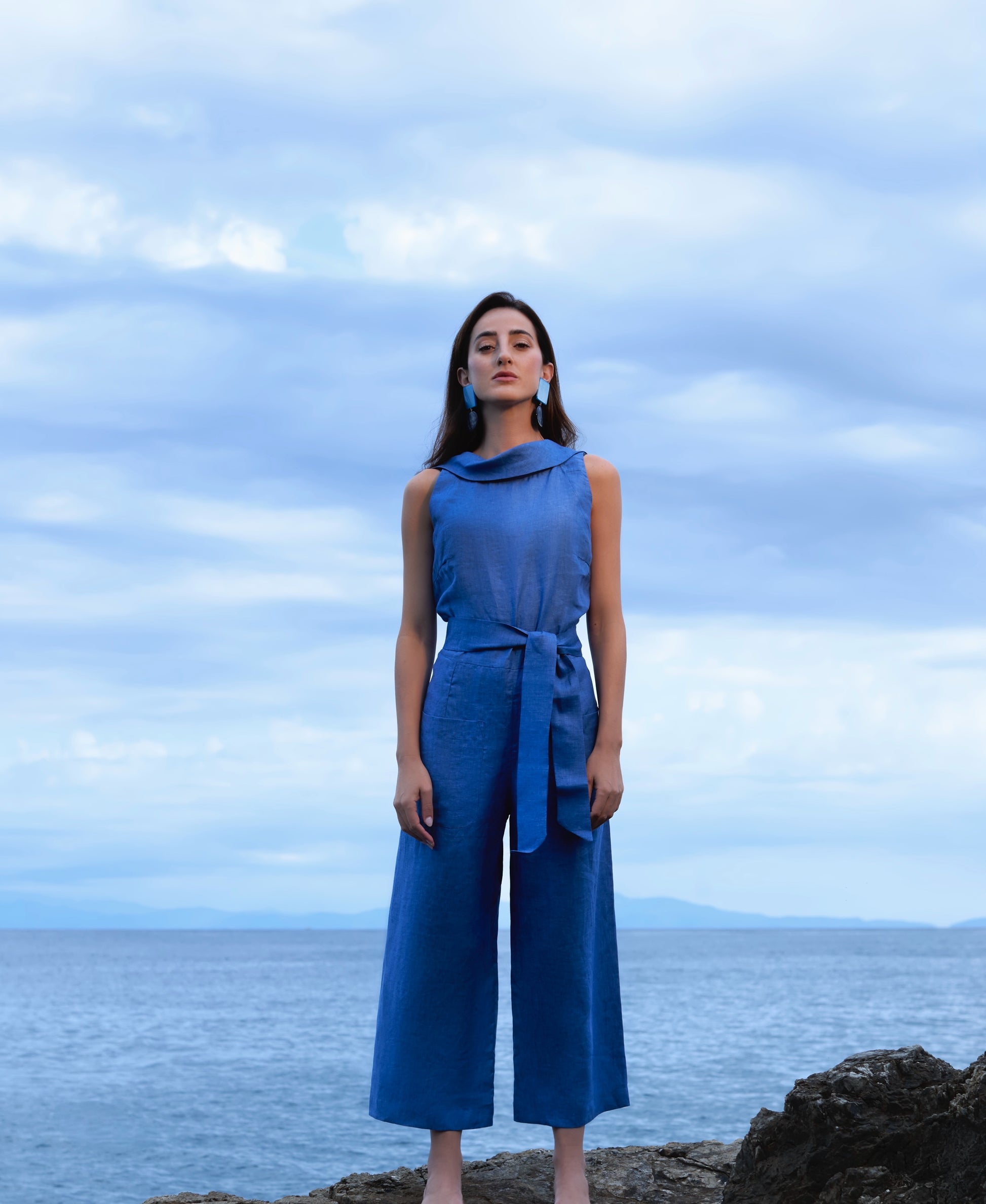 Woman in a blue outfit standing on a rocky outcrop with a cloudy sky and ocean background Blue Royal