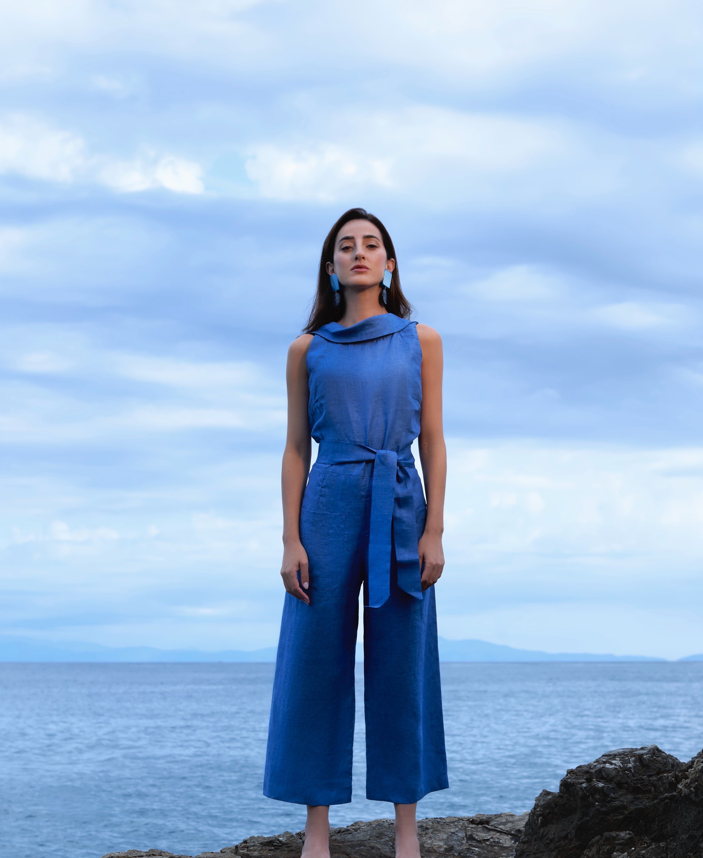 Woman in a blue outfit standing on a rocky outcrop with a cloudy sky and ocean background Blue Royal