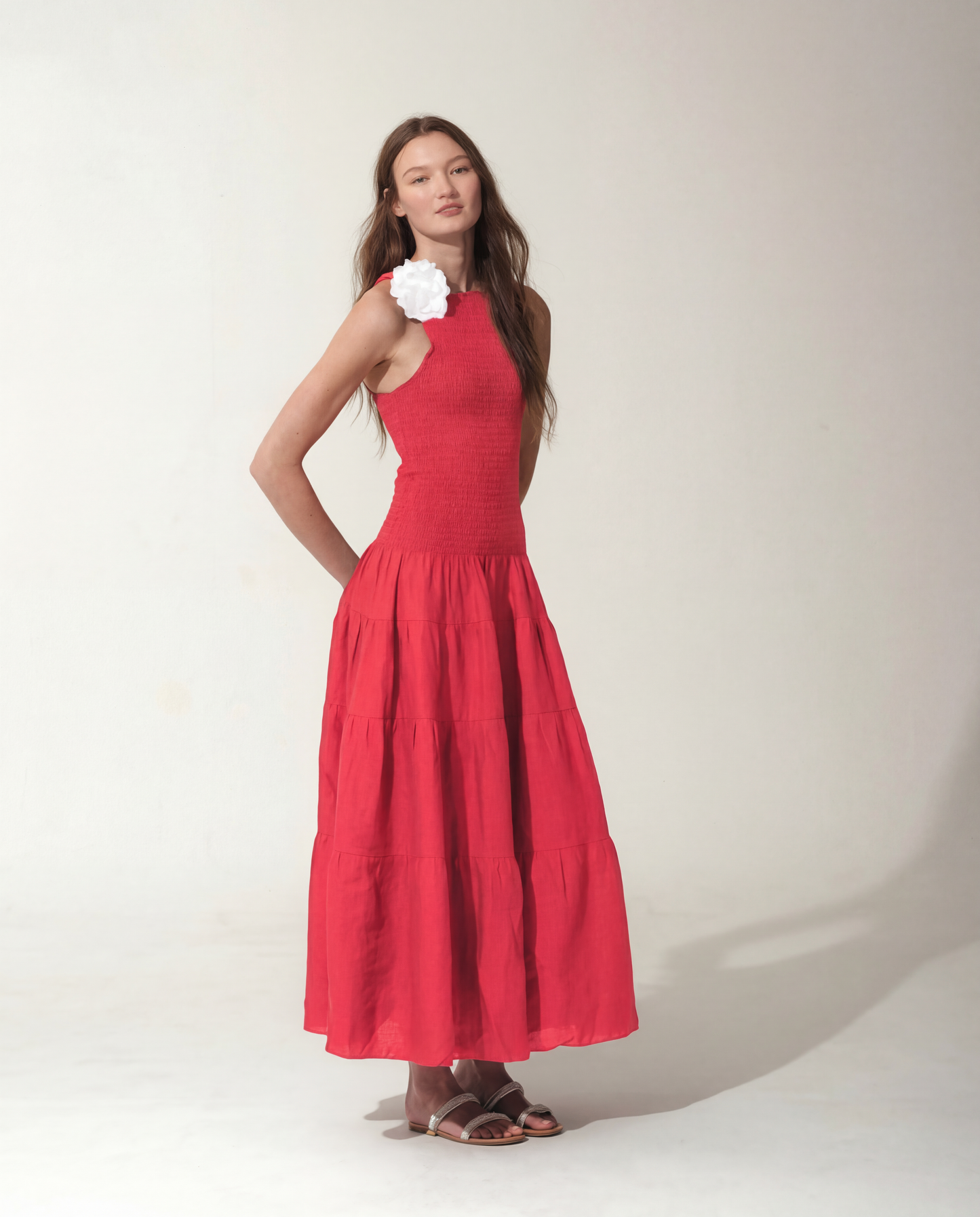 Woman wearing a Strawberry Red dress with a flower detail on a plain background