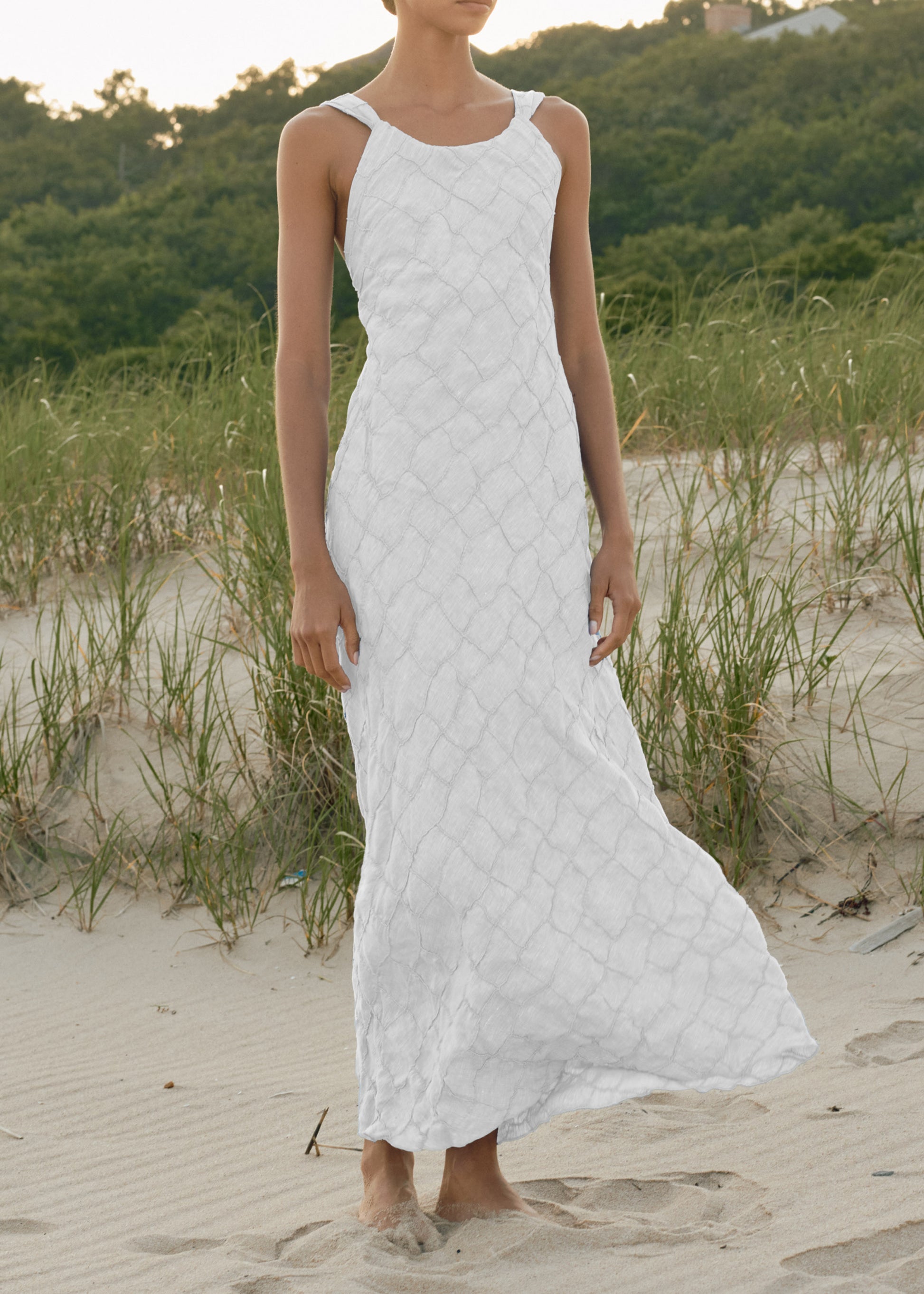 Woman wearing a White quilted dress on a sandy beach with greenery in the background