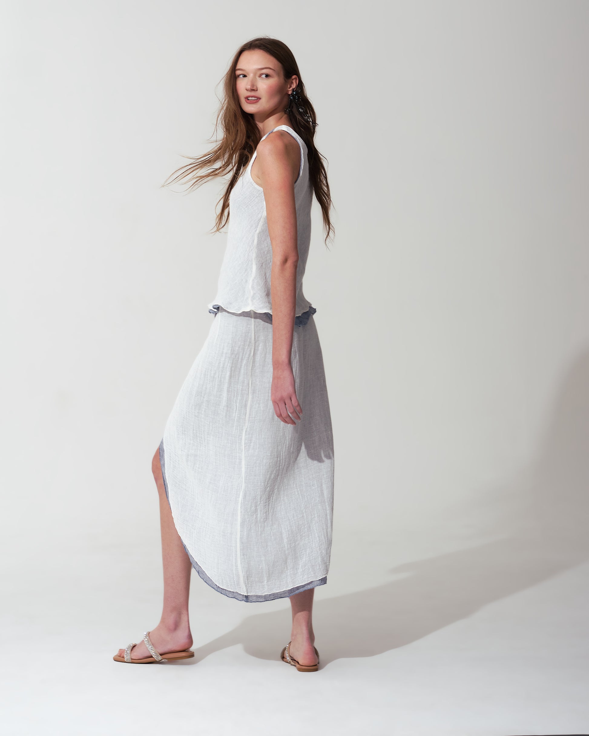 Woman wearing a White dress with a high slit on a plain background