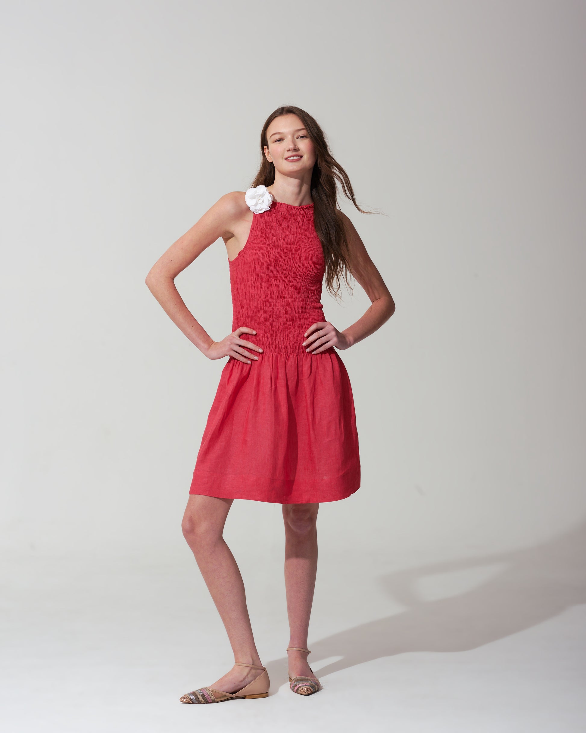 Woman wearing a strawberry red dress with a  flower on a plain background
