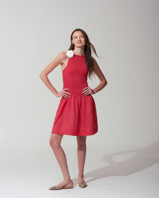 Woman wearing a strawberry red dress with a  flower on a plain background