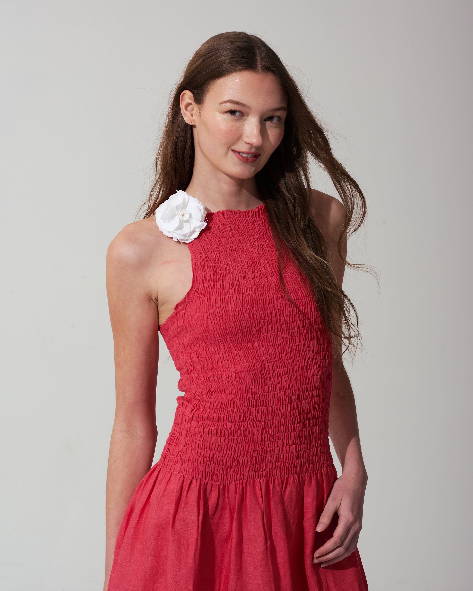Woman wearing a strawberry red dress with a white floral detail on a background
