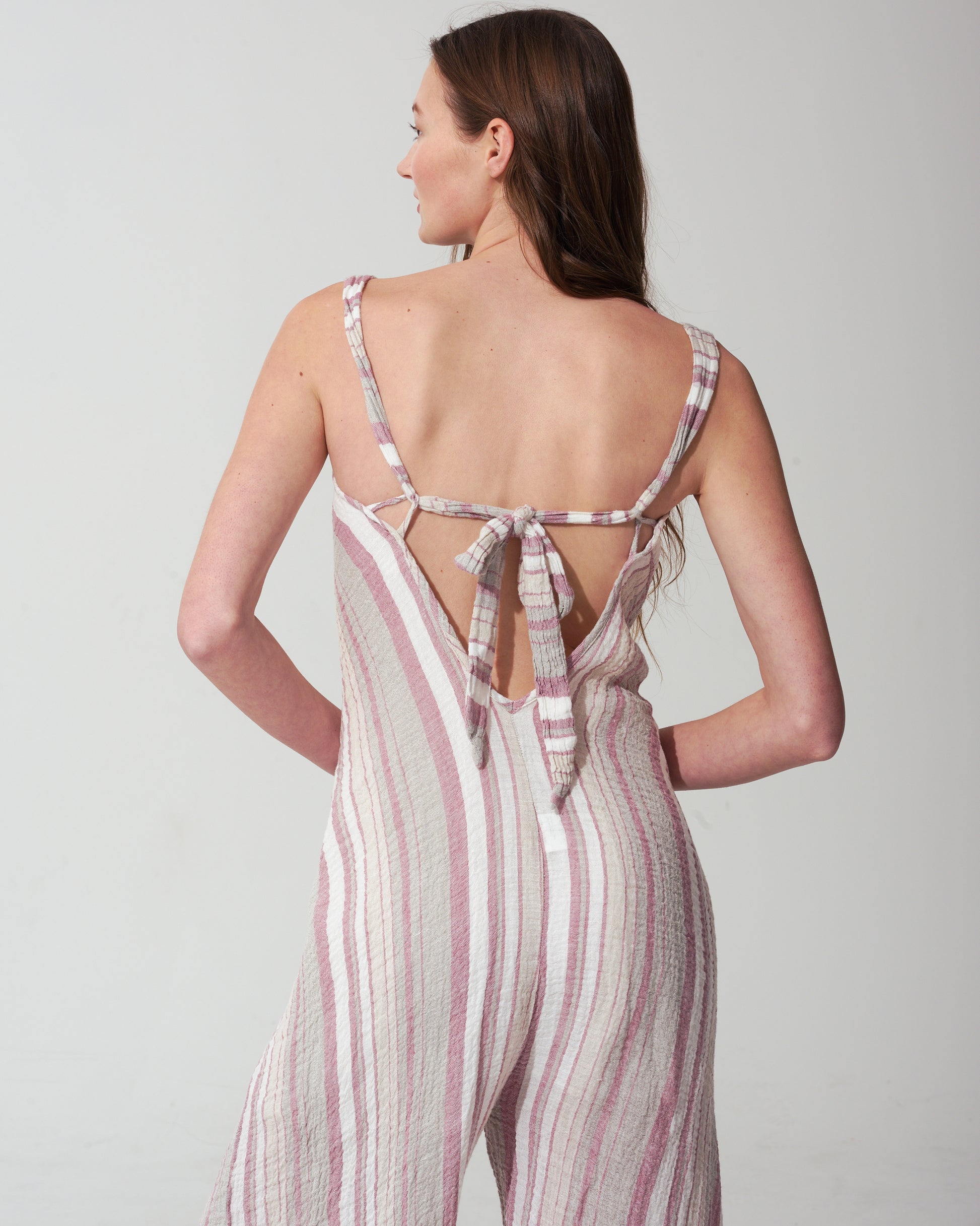 Woman wearing a striped pink jumpsuit with an open back on a plain background