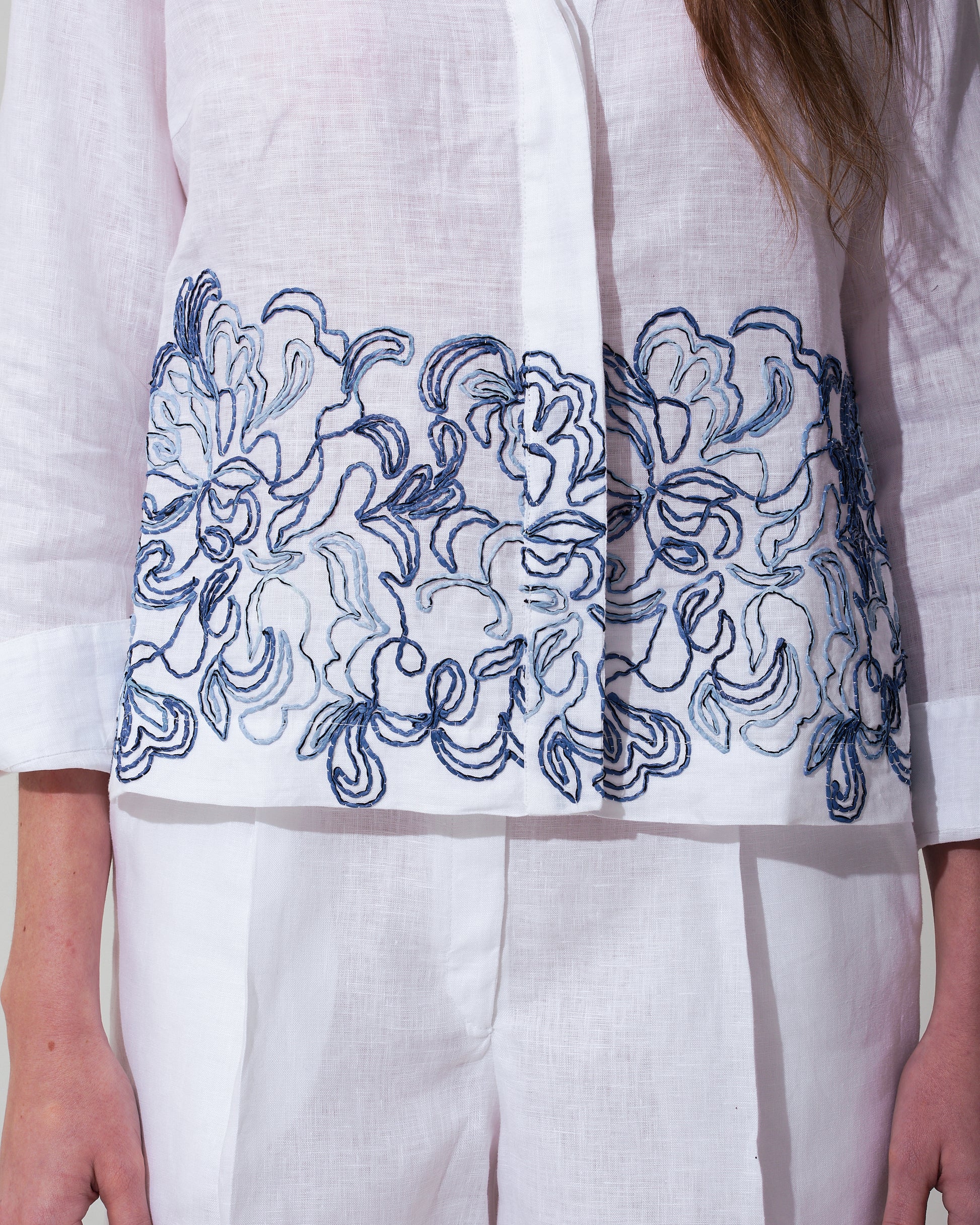 White garment with blue raffia floral embroidery on a plain background