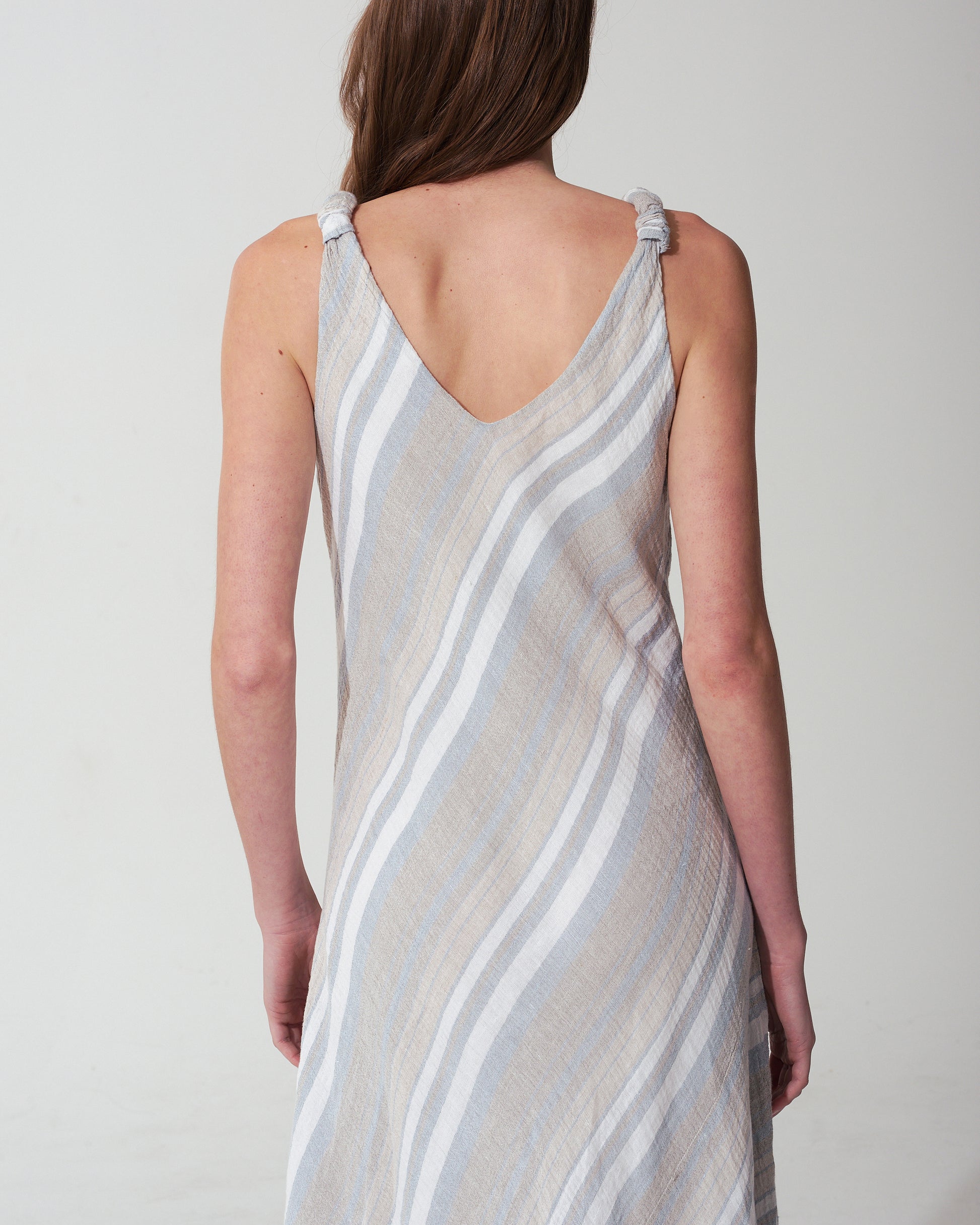Woman wearing a striped blue dress with thin straps on a plain background