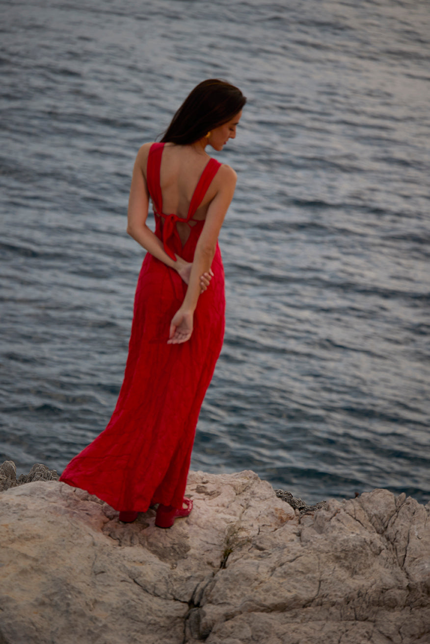 Woman in a Red dress standing on rocks by the water